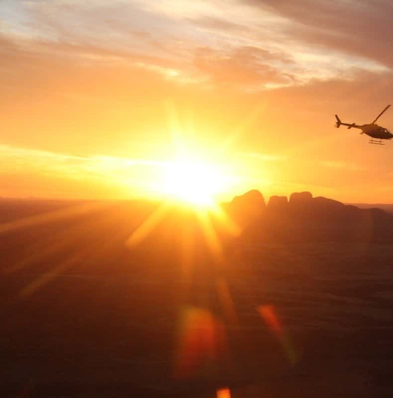 A helicopter silhouetted against the setting sun over the desert