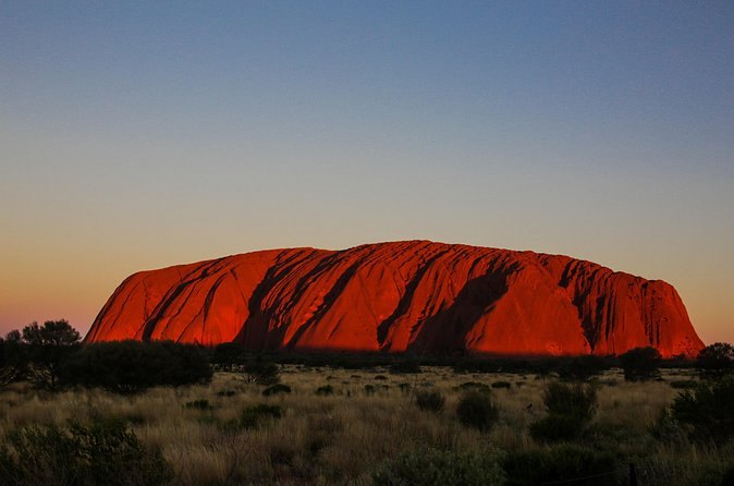 Uluru turning deep red as the sun drops behind the plain