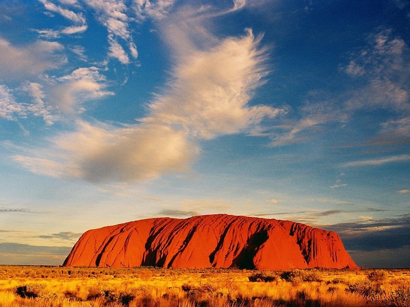 Uluru low on the horizon under a wide bank of desert cloud